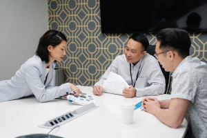 Three colleagues from an Malaysian SME in a meeting, appearing hesitant, about investing in safeguards against transfer-pricing risks
